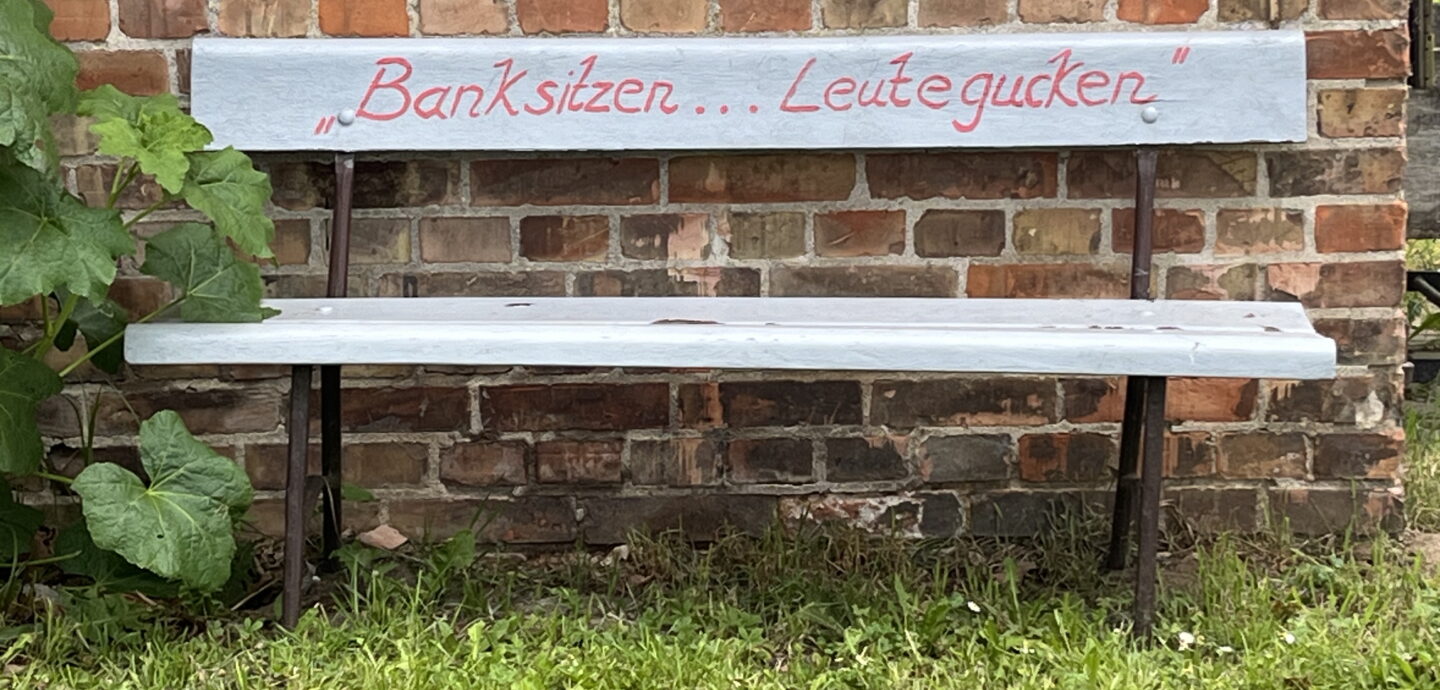 weiß gestrichene Bank mit der Aufschrift "Bank sitzen Leute gucken" vor Backsteinmauer © K. Schwahlen 2024